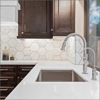 closeup of stainless steel faucet with brown cabinets and white counters