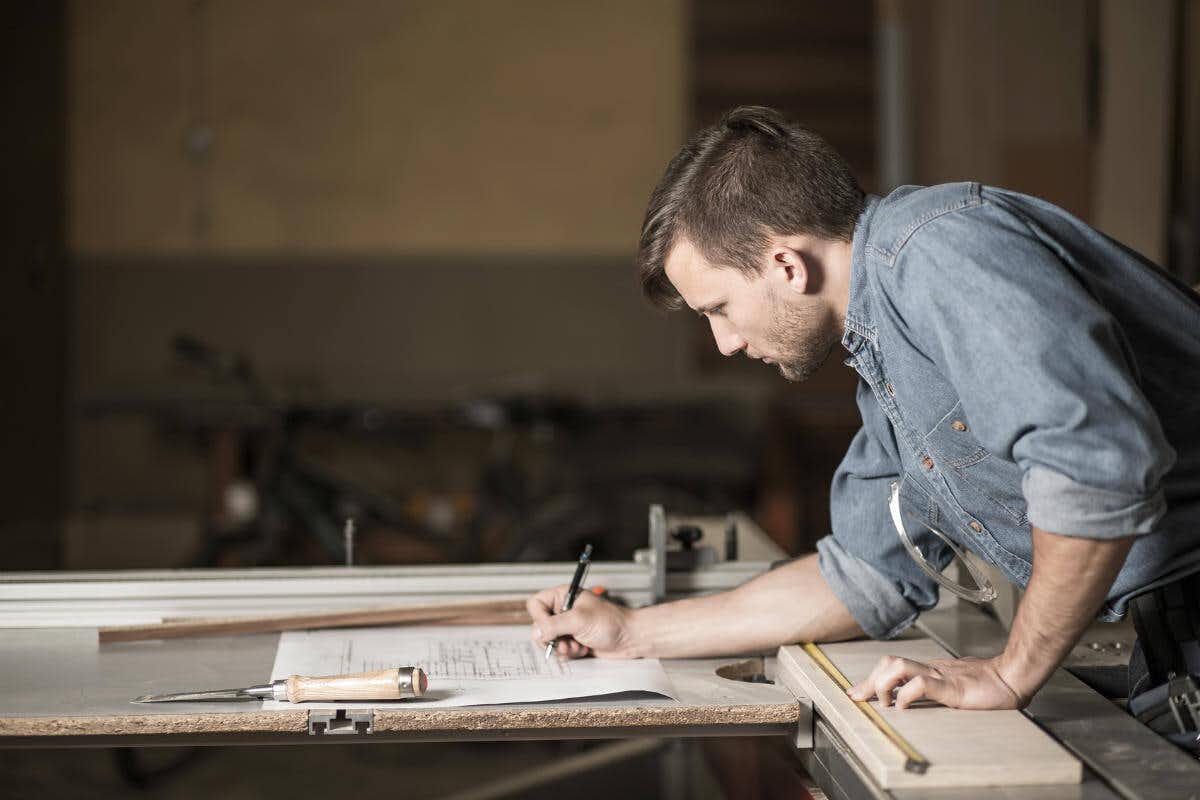 man writing blueprints on wooden desk